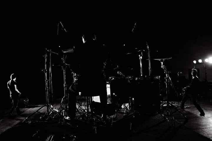 Dramatic black and white backstage view of a band performing live on stage.