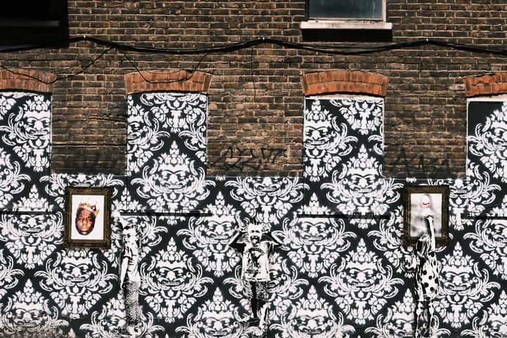A richly textured street art mural with ornate patterns and framed portraits on a brick wall.