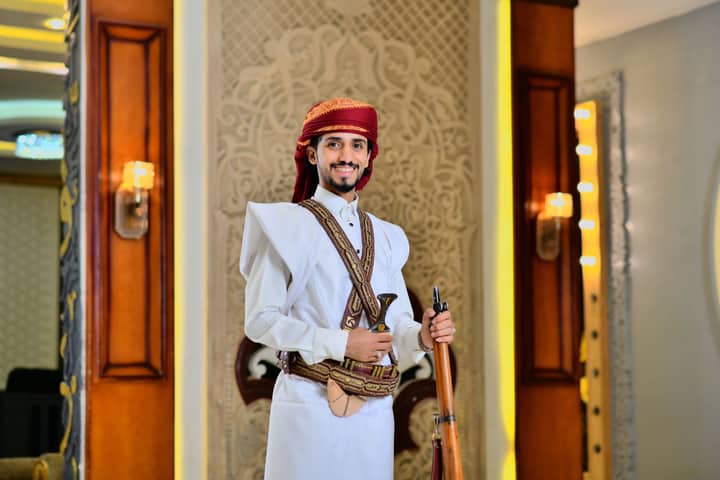 Man in traditional Saudi Arabian attire with ornate decor in Makkah Province setting.