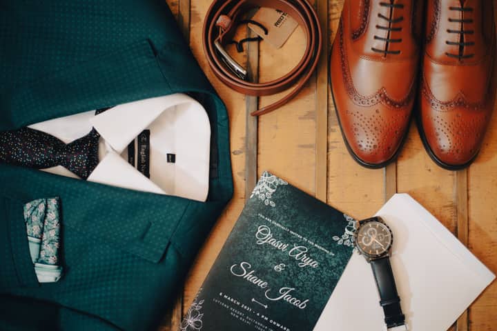 Classic men's wedding accessories flat lay featuring suit, shoes, and invitation.