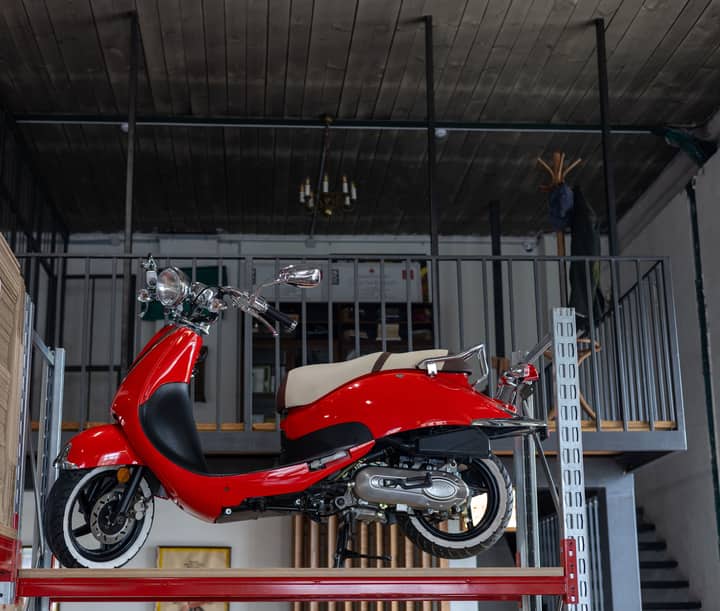 Bright red scooter displayed in a modern industrial loft space, showcasing sleek design.