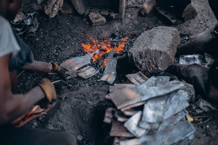 Blacksmith forging metal over an open fire, showcasing traditional craftsmanship.