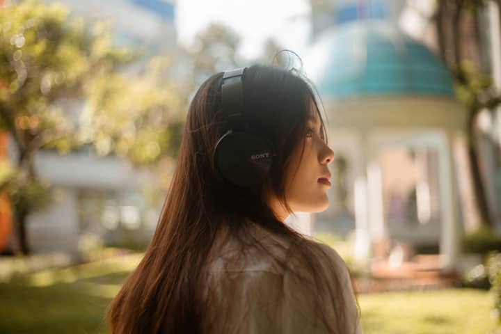 Young woman enjoying music with headphones in a sunny outdoor park.