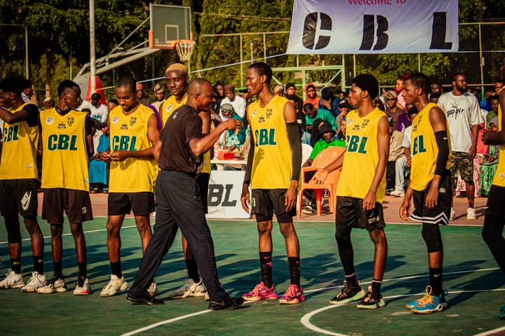 A basketball coach speaks with players during an outdoor game on a sunny day.