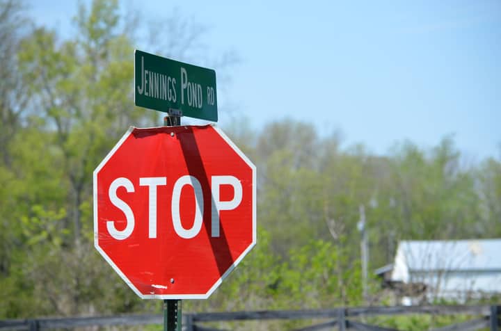 A stop sign and road sign on Jennings Pond Road in a rural setting with trees and blue sky.