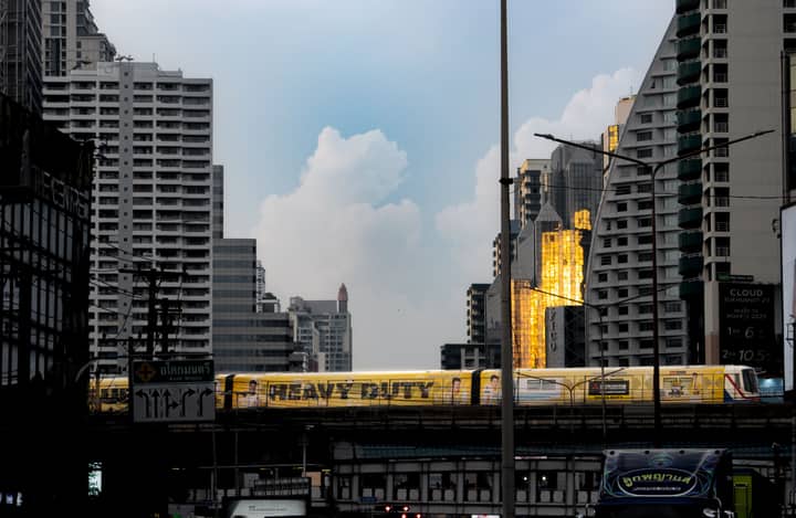 Cityscape featuring Bangkok's skytrain with golden reflections on skyscrapers at sunset.