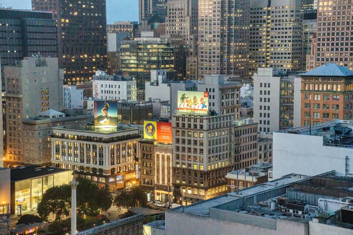 A vibrant view of San Francisco's downtown skyline at dusk with illuminated buildings and billboards.