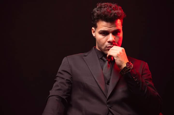 Portrait of a thoughtful man in a black suit with a red light accent in a moody setting.