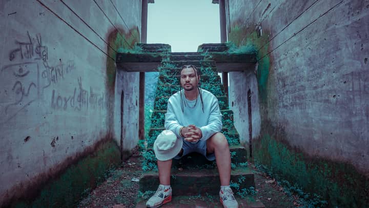 A stylish young man sits on mossy steps in Rishikesh, India, showcasing urban fashion.