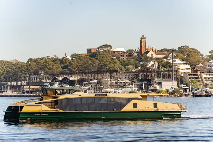 A ferry glides by Barangaroo with cityscape and lush greenery in the background.