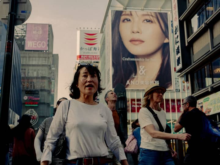 A lively street scene in Japan featuring diverse pedestrians and prominent billboards.