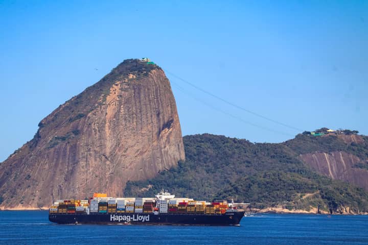 Container ship passing by Sugarloaf Mountain in Rio de Janeiro on a clear day, showcasing global trade.