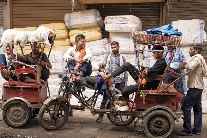 Rickshaw drivers taking a break in the bustling market of Delhi, India, surrounded by goods and vibrant street life.
