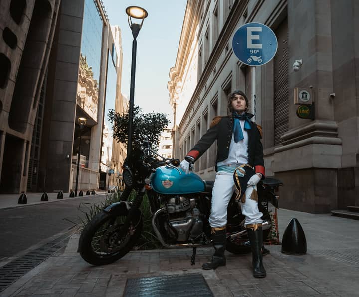 Young man in a historical costume poses with a motorcycle on a street in Buenos Aires.