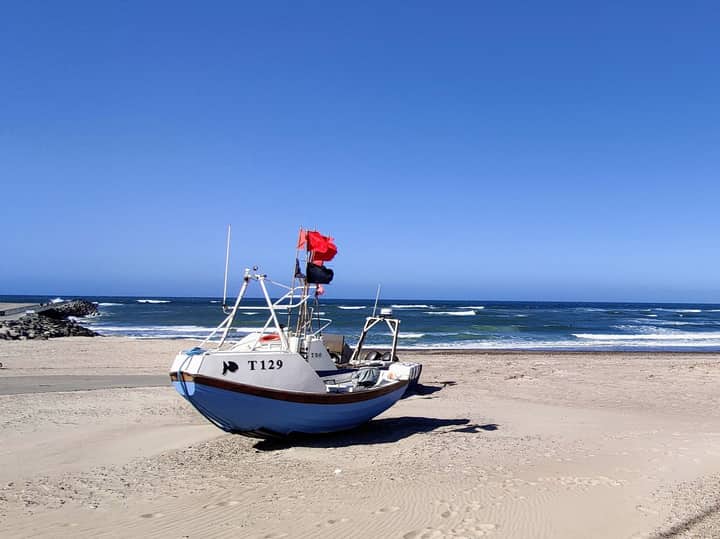 Fishing boat on a sandy beach under a clear blue sky, showcasing the calm sea and coastline.