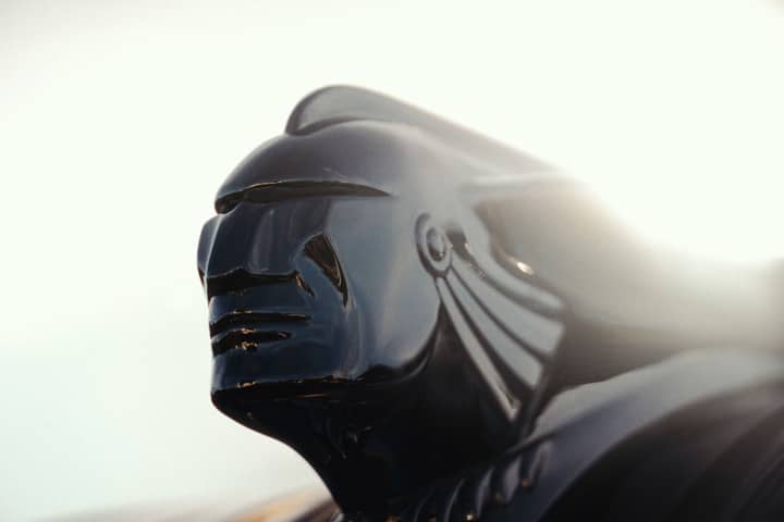 Dramatic close-up of a vintage car hood ornament, highlighting its intricate design under bright light.