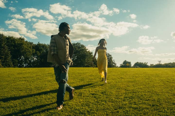 A man and woman walking on a grassy field under a bright sky, capturing a warm summer day.