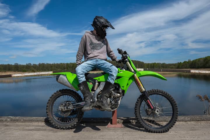 A motorcyclist on a green dirt bike, enjoying a peaceful day by the lake.