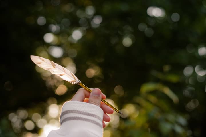 A hand holds a quill pen with a soft bokeh effect, evoking creativity and inspiration.