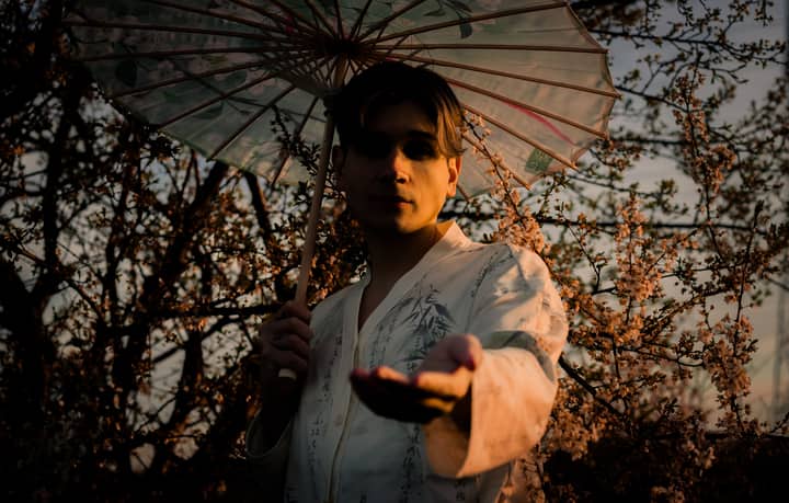 Artistic portrait of a young man in a kimono with a parasol among cherry blossoms.