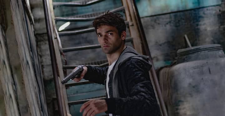 A man holding a gun in a dimly lit, mysterious urban setting.