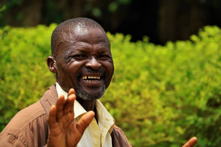 African man smiling joyfully in a vibrant green outdoor setting in Uganda.
