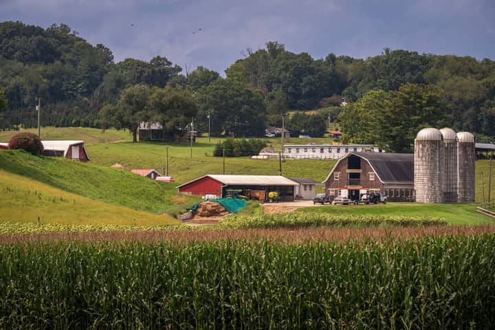 Beautiful rural farm landscape showing barns, silos, and lush greenery under a clear sky.