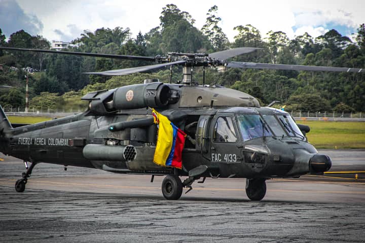 Colombian military helicopter on tarmac with national flag visible.