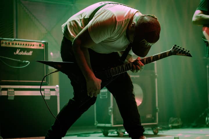 A dynamic guitarist bends forward in a passionate performance on stage with electric guitar and amplifiers.