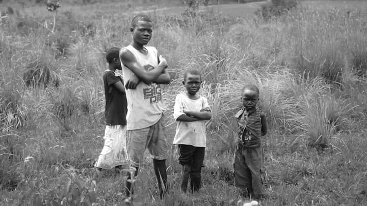 A group of children stands in a grassy field in Bunia, Congo, posing for a black and white portrait.