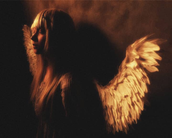 Moody portrait of an angelic figure with glowing wings, evoking mystery and serenity.