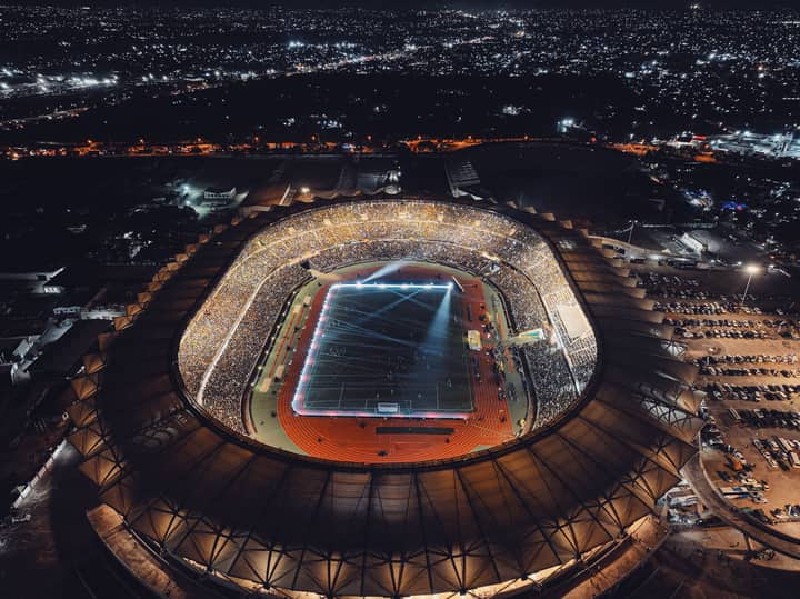 Vibrant night view of a brightly lit stadium in Dar es Salaam during a soccer match with a full crowd.