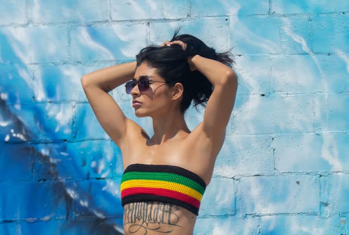 A fashionable woman in vibrant clothing poses confidently against a colorful wall in Ceará, Brazil.