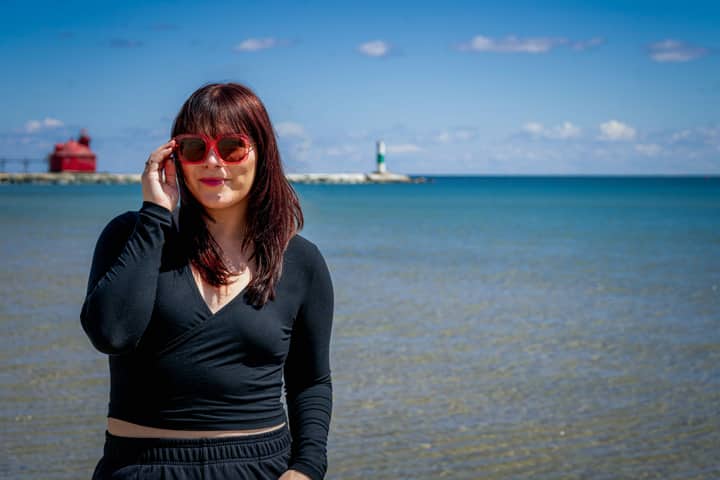 Portrait of a woman in stylish attire by Sturgeon Bay with scenic lighthouse view.