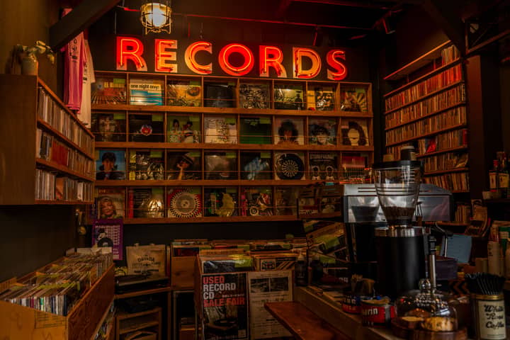 Warm interior view of a record store with vintage vinyls, retro decor, and a neon 'Records' sign.