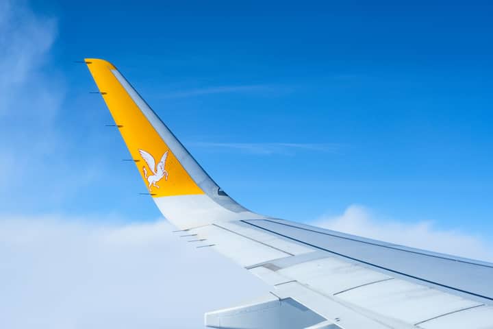 Airplane wing with airline logo flying above the clouds on a clear day.