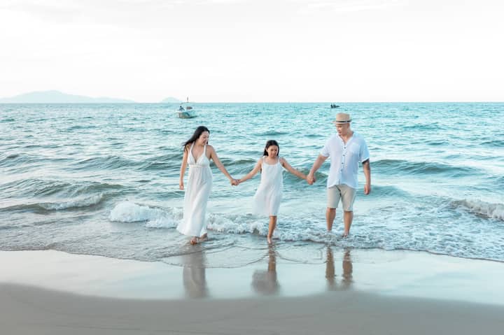 A joyful family of three walks hand-in-hand along Hội An beach, enjoying a sunny day.