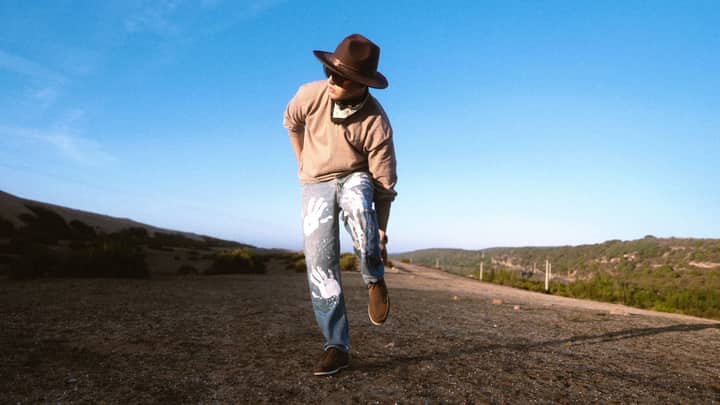 Casually dressed man in hat and sunglasses poses on a sunny day outdoors.