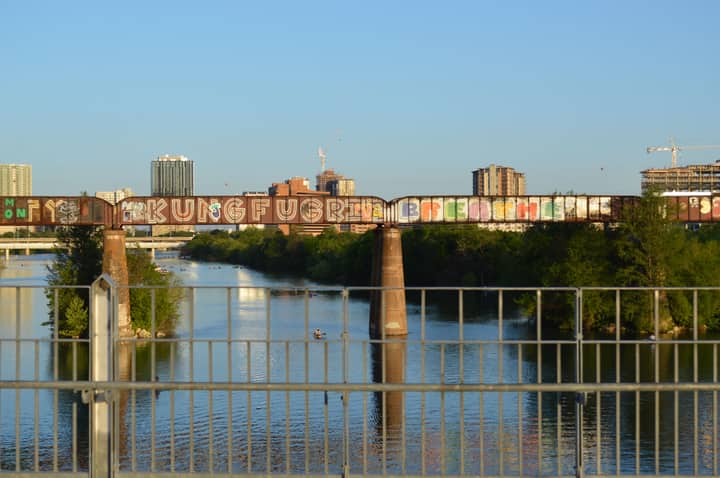 Colorful graffiti on a bridge over Lady Bird Lake with Austin skyline in the backdrop.