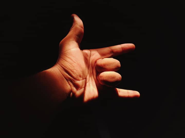 A close-up of a hand making the shaka sign, dramatically lit against a dark background.