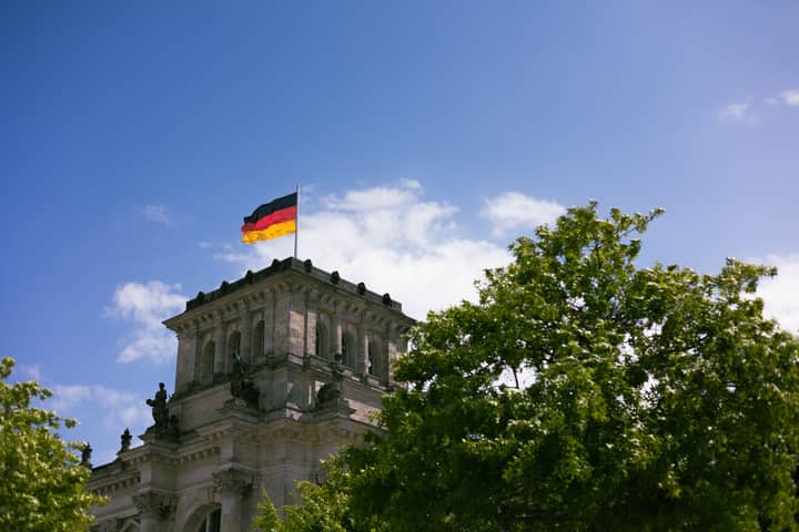 The iconic Reichstag in Berlin with the German flag flying high against a clear blue sky.