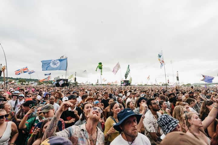 A lively crowd enjoying the Glastonbury Festival in England, with flags waving across the sky.