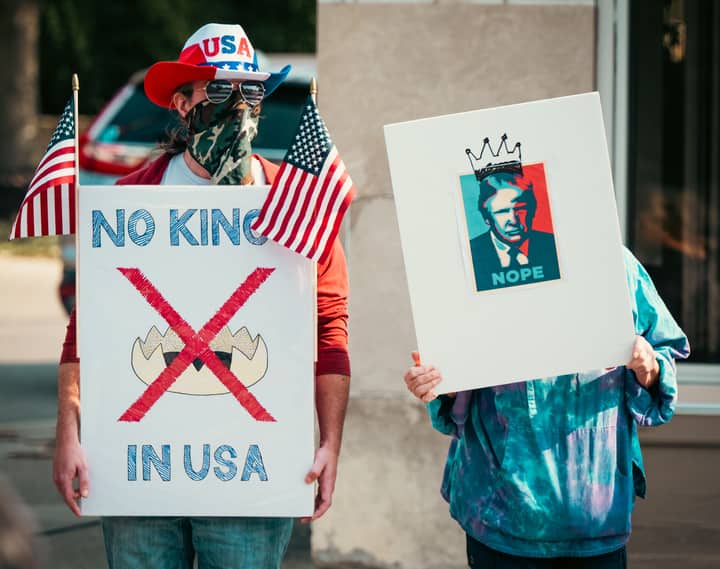 Two protesters displaying political signs during a demonstration with US flags.