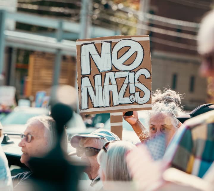 A vibrant anti-fascist protest features a crowd holding a NO NAZIS sign outdoors.