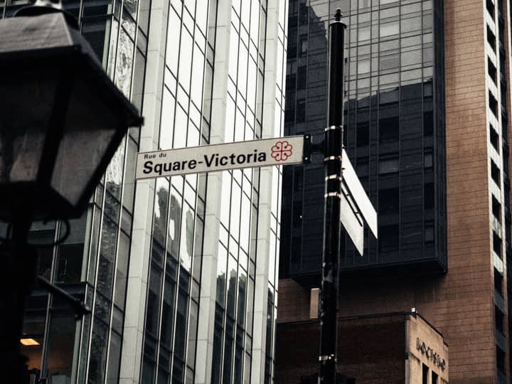 Street sign for Rue du Square-Victoria in Montreal, set against a backdrop of modern architecture.
