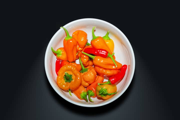 A vibrant collection of orange and red peppers in a white bowl, showcasing fresh organic produce.