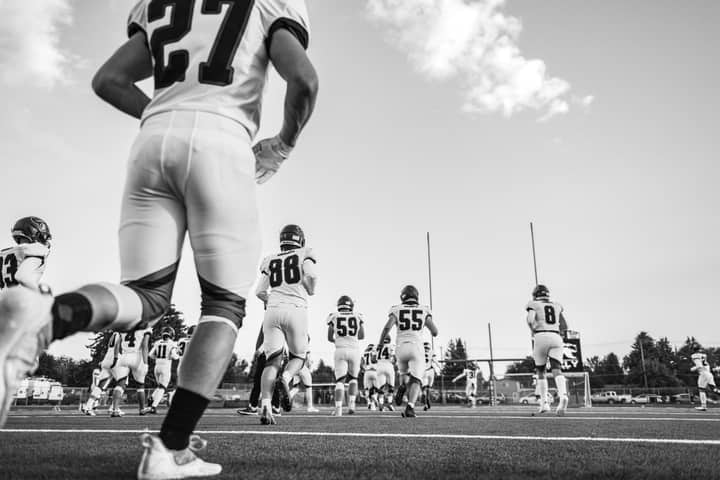 Dramatic black and white photo capturing high school football players in action on the field.