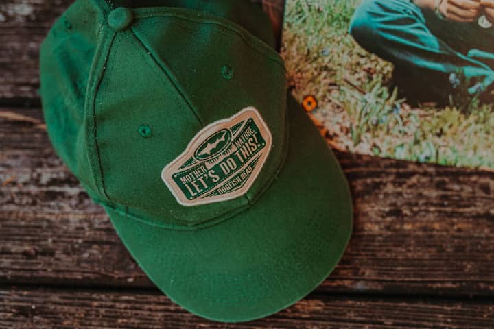Close-up of a green adventure hat with text, resting on a wooden surface outdoors.