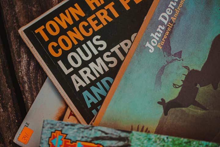 Close-up of vintage record covers showcasing John Denver and Louis Armstrong, Alabama setting.
