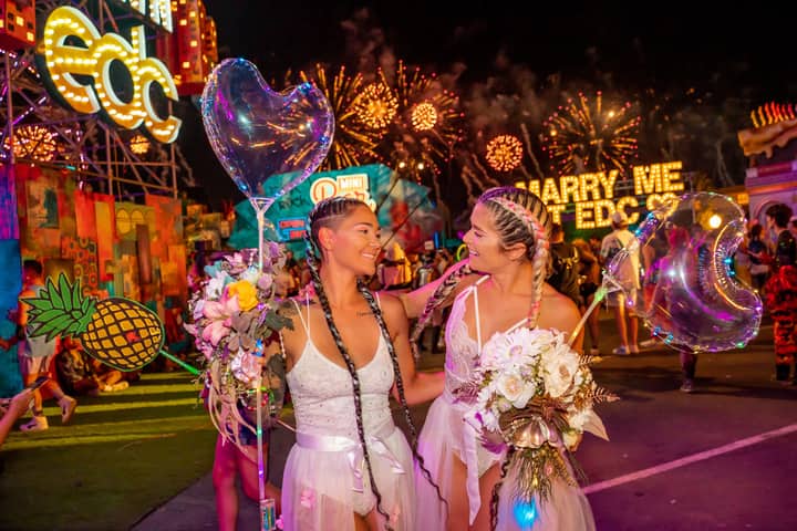 Two women celebrating at a vibrant music festival with fireworks and lights.